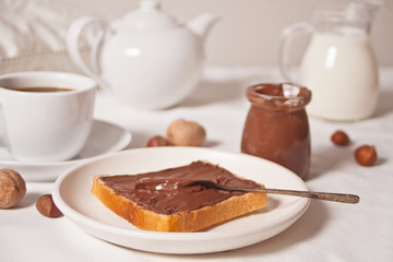 Bread toast with chocolate cream butter, jar of chocolate cream, cuop of tea, jar of milk, teapot on the white background.