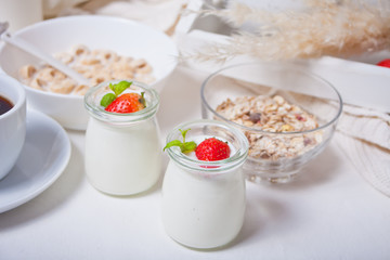 Two portions natural homemade yogurt in a glass jar with fresh strawberry and muesli nearby