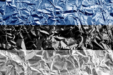 Estonia flag depicted in paint colors on shiny crumpled aluminium foil closeup. Textured banner on...