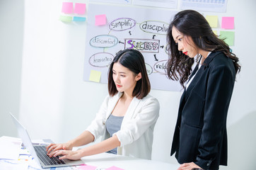 Two asian hardworking young female entrepreneurs working together on a laptop computer reading the screen with serious engrossed expressions, Agile scrum concept