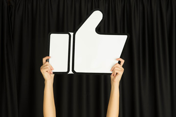 Hands holding the sign of like on black studio background. Negative space to insert your text or image, advertising. Social media, showing meaning, communication, gadgets, modern technologies.