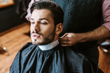barber fixing collar around neck of man in barbers cape