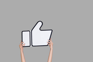 Hands holding the sign of like on grey studio background. Negative space to insert your text or...