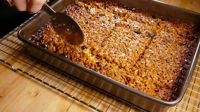 Hands using a rolling cutter to slice a freshly baked tray of flapjack (oat bar / cereal bar / muesli bar).