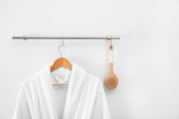 Hanger with clean bathrobe and brush on light wall - obrazy, fototapety, plakaty