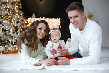 A happy family, father, mother and little daughter, spend time together on Christmas evening in a...