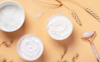 White cream, salt in the bowl, gua sha roller, spikelets of wheat and oats on a beige background, top view. Body and skin care at home concept. Ingredients for scrub with salt flat lay.