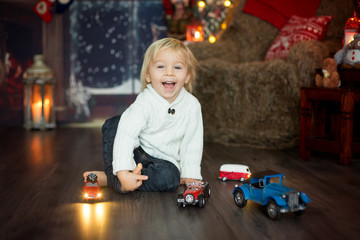 Cute toddler boy, sitting around many car toys on the floor, playing