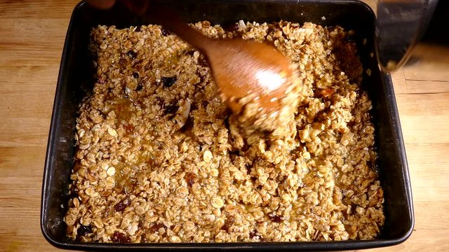 Hands scooping flapjack (oat bar / cereal bar / muesli bar) mix from a pan into a baking tray, ready for the oven.