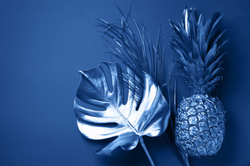 Painted exotic fruits, tropical palm, monstera leaves on classic blue background. Top view. Flat...