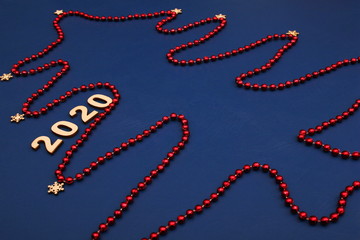 2020 Happy New Year. A Christmas tree made of red Christmas beads is laid out on a blue background.