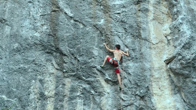 slow motion back view muscular man rock climber carefully climbing on a high vertical limestone cliff. outdoor climbing moments
