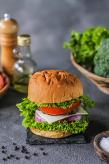 Photo of fresh burger on wooden cutting board on dark background..Homemade hamburger with beef, onion, tomato, lettuce and cheese. Homemade fast food. Dark textured background. Copy space. Image.