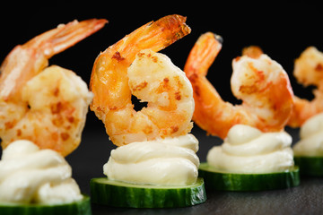 Delicious sauteed shrimp on cream cheese and sliced cucumber. black background closeup