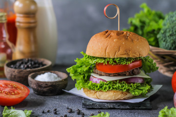 Photo of fresh burger on wooden cutting board on dark background..Homemade hamburger with beef, onion, tomato, lettuce and cheese. Homemade fast food. Dark textured background. Copy space. Image.