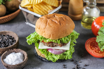 Photo of fresh burger on wooden cutting board on dark background..Homemade hamburger with beef, onion, tomato, lettuce and cheese. Homemade fast food. Dark textured background. Copy space. Image.