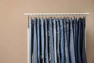 Rack with stylish jeans on beige background