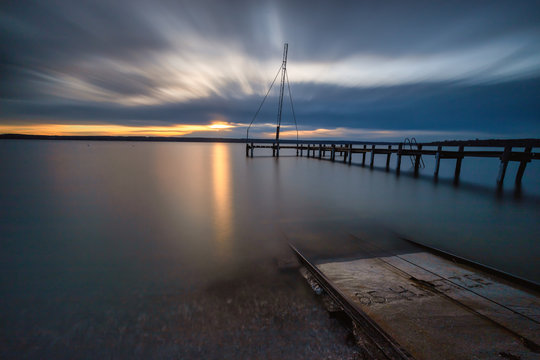 Sonnenuntergang am Ammersee mit Steg und Schienen die ins Wasser f&uuml;hren