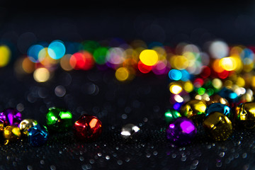 Colorful Christmas jingle bells. Black blurred bokeh glitter background. Shallow depth of field. For overlay, background or texture.