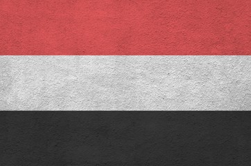 Yemen flag depicted in bright paint colors on old relief plastering wall. Textured banner on rough...