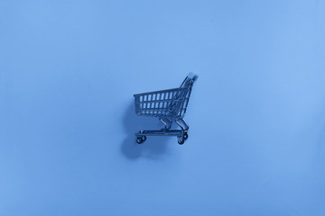 Shopping cart on classic blue background. Minimalism style. Shop trolley at supermarket. Trendy...