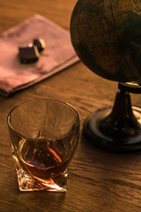 Glass of brandy with globe and lighter on map on wooden table