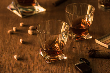 Glasses of brandy with pistachios, cigar and lighter on wooden table