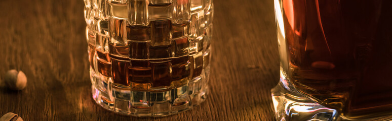 Glass of brandy with decanter and pistachios on wooden table, panoramic shot