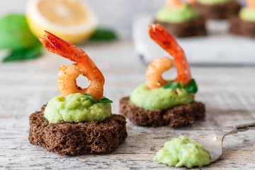 Canapes with avocado mousse and spicy shrimp on brown bread