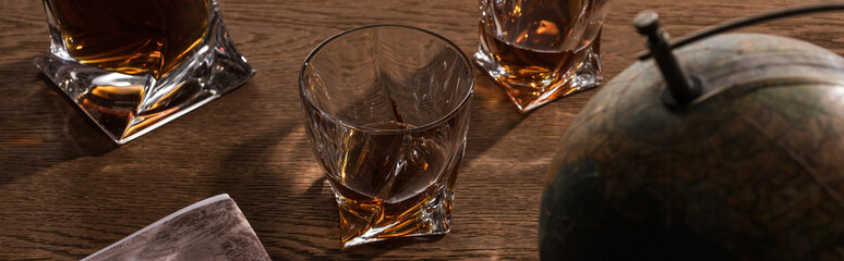 Selective focus of brandy in glasses with globe and map on wooden table, panoramic shot