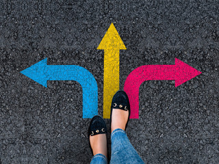woman legs in shoes standing on road with three direction arrow choices, left, right or move forward