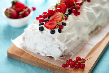 Close-up sponge biscuit cake roll filling whipped cream and berries decorated strawberry, blueberry and red currants on turquoise background. Soft focus. Summer food concept