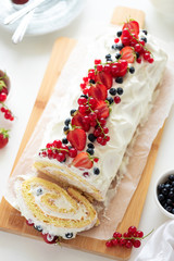 Cutted sponge (biscuit) cake roll filling whipped cream and berries decorated strawberry, blueberry and red currants on white wooden background. Soft focus. Summer food concept