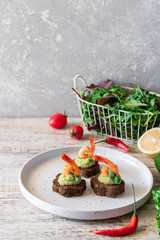 Canapes with avocado mousse and spicy shrimp on brown bread
