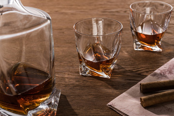 Glasses of brandy with decanter and cigars on map on wooden table