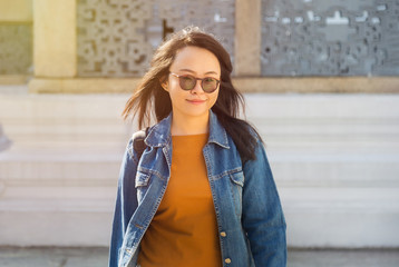 Fototapeta premium Close up portrait glasses Asian woman with smile in t- shirt and jeans jacket with backpack looking at camera inside Wat Phra Kaew The Grand palace favorite place of Bangkok Thailand