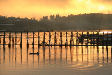 A little boat and wooden bridge with mountain landscape over the river at Sunrise in Thailand.