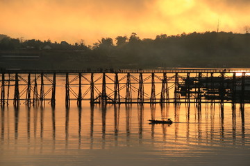 Obraz premium A little boat and wooden bridge with mountain landscape over the river at Sunrise in Thailand.