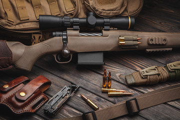 Modern bolted carbine and cartridges for it on a dark wooden table. Rifle with a telescopic sight on a dark background. Weapons for hunting, sports and self-defense. Postcard concept.