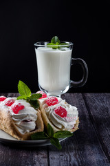 Kefir is decorated with a leaf of mint, a fermented drink. Air cake on a saucer. wood background