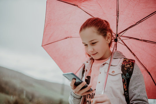 Little Girl Waiting For Bus On Rain Day And Using Phone