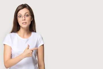 Confused young woman showing aside with finger to copyspace place