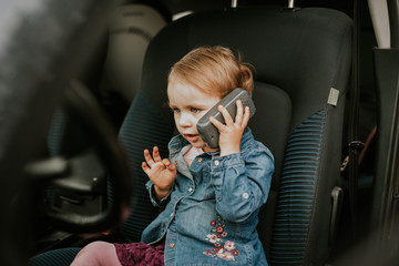 Little girl in a car seat. Holding phone in her hand. Taking driver seat. Car damage. Authentic image