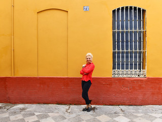 Caucasian white woman posing near colorful building exterior in Bario Santa Cruz in Seville, Spain. Colorful buildings in jewish area in Seville