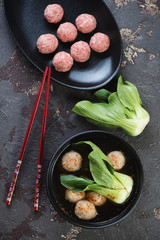 Asian meatball soup with bok choy, top view over brown stone background with uncooked meatballs, vertical shot