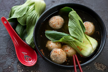Miso soup with meatballs and pak-choi served in a black bowl, studio shot over brown stone surface
