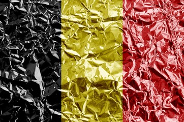 Belgium flag depicted in paint colors on shiny crumpled aluminium foil closeup. Textured banner on...
