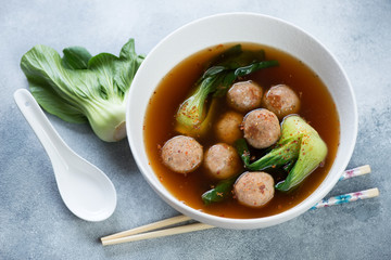 Bowl of meatballs and pak-choi in miso broth, studio shot over light-blue stone background
