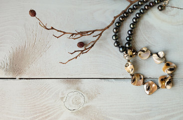 Women's beads made of black pearls and nacre and a branch with berries on a blue wooden table. Composition with jewelry, top view, place for an inscription, open space