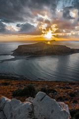 The sun sets in clouds behind a small island